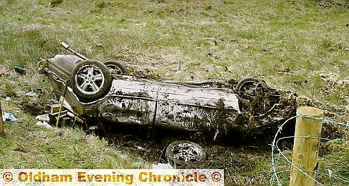 THE overturned, mangled wreckage of the car lies in a peat bog at the side of the Greenfield to Holmfirth road 