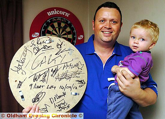 ON CLOUD NINE: Paul Cartwright, with son Archie, shows off the signed board presented to him after his superb nine-dart finish. 