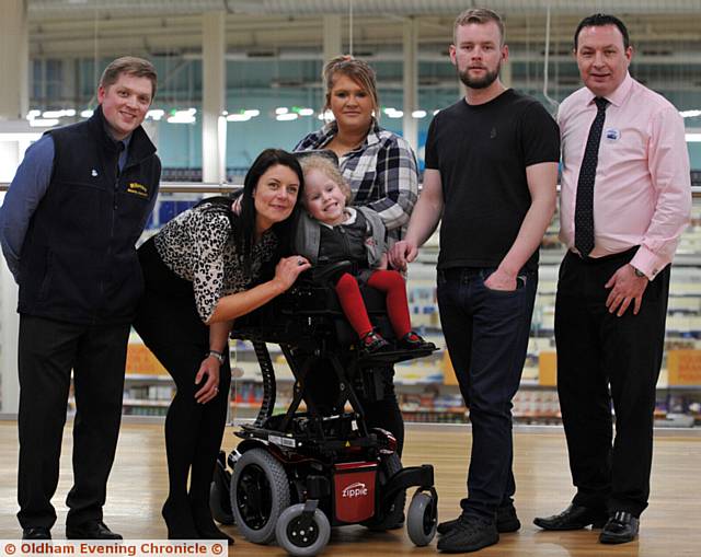MILLIE receives her new wheelchair from Millercare at Tesco, Huddersfield Road in Oldham. Pictured, from left, Andy Walker (Millercare), Marie Toora (Tesco, Westwood Manager), Millie, Emma-Jayne Clarke (Millie's mum), Michael Moran (Millie's dad), Andrew Brown (Tesco, Oldham manager) 
