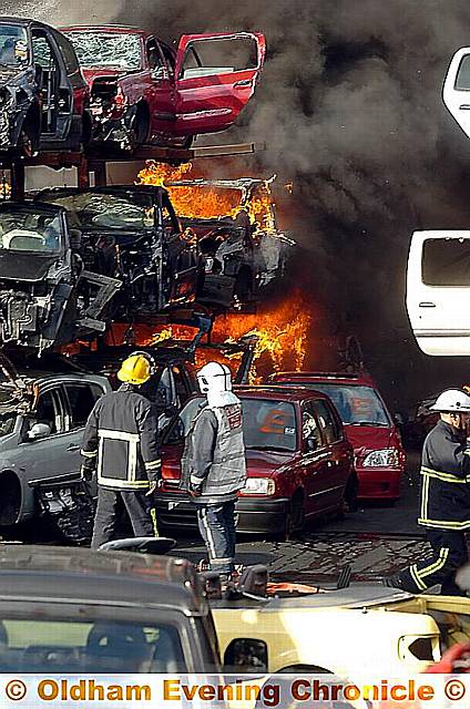 Fire-fighters in front of a burning stack of cars at Broadbent Autos