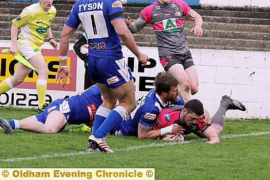 Oldham’s Jack Holmes dives for the line with two Barrow players for company.
