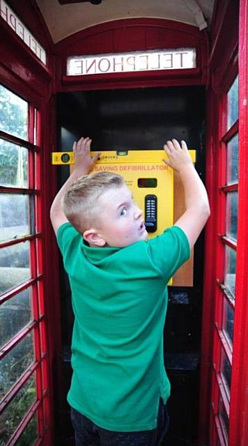Teddy Royle (10) installs defibrillator in former phone box in Ladcastle Road Dobcross