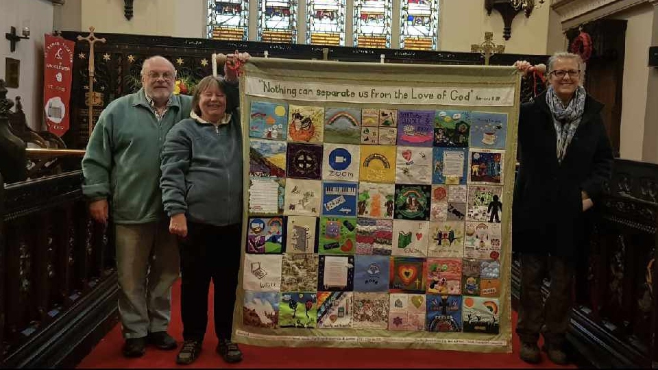 Janet is pictured with the banner, her husband Geoff and Canon Jones