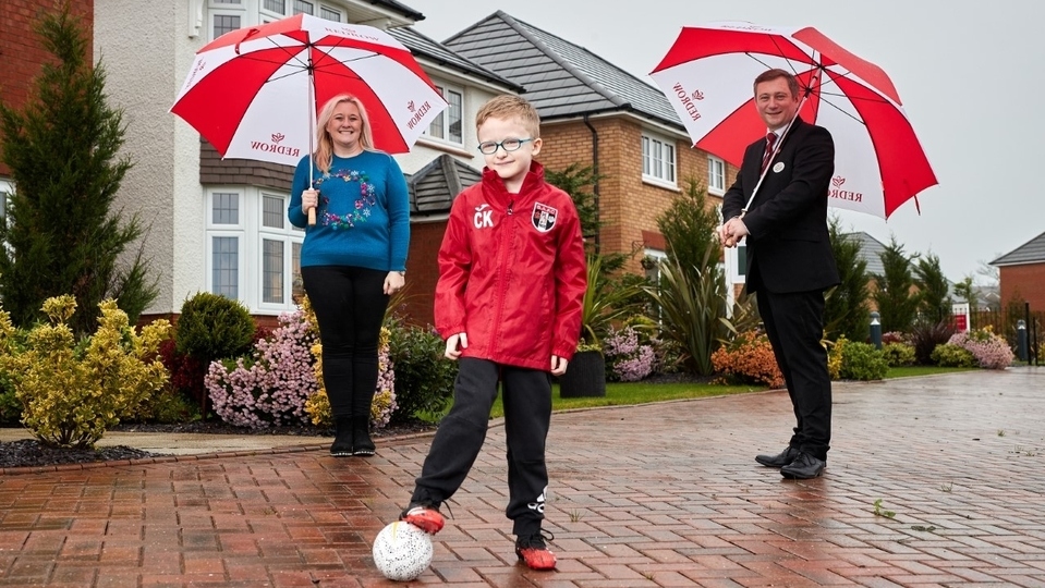 Charlie Kearney from Springhead AFC poses in his new kit funded by Redrow, with mum Felicity Kearney and Redrow sales consultant Michael Deegan at Saddleworth View (photo taken pre-national lockdown)