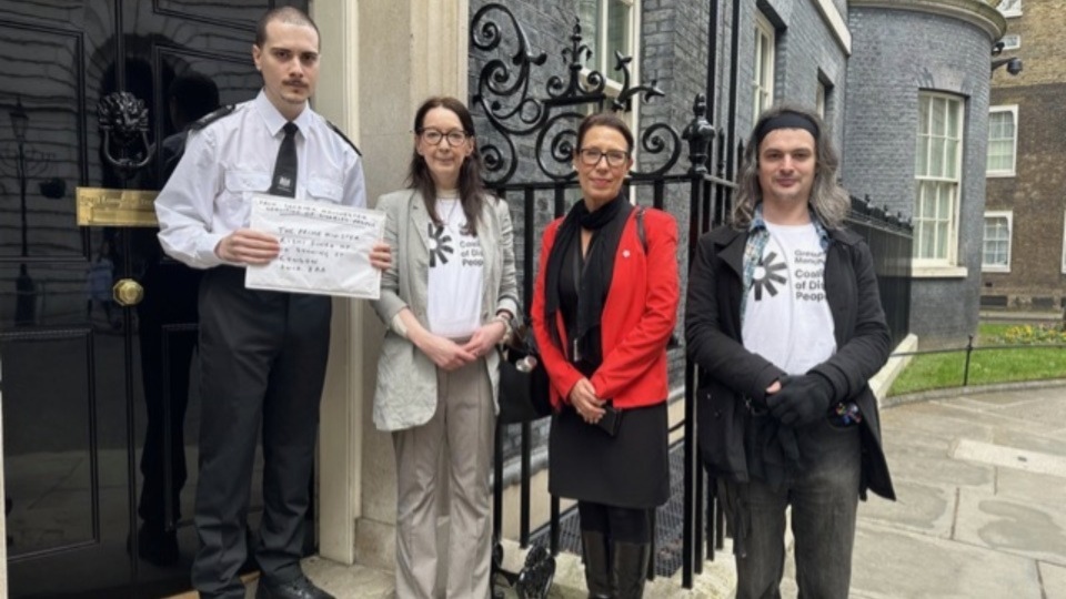 Pictured (left to right): A Downing Street security guard accepts the petition from Helen Rowlands, representing the Greater Manchester Coalition of Disabled People; Debbie Abrahams, MP for Oldham East and Saddleworth; and Pete Marshall, also GMCDP