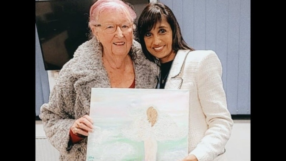 Visiting Angels Managing Director Roxie Taj is pictured with warm-hearted client Sheina Burns, and her painting