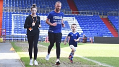 NorthCare Charity fundraiser Tim Greenwood (centre) completes his 300-mile run at Oldham Athletic AFC ground Boundary Park, flanked by his children Isabelle, 13, and Noah, 5.