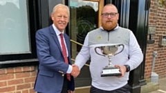 Adam Rowbotham receives the District Championship trophy from Dion Norbury, captain of host club Crompton and Royton